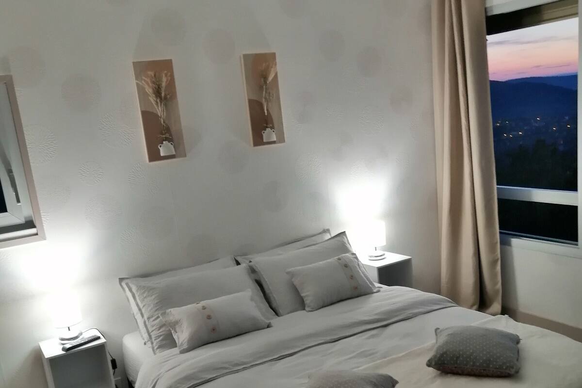 Une chambre à coucher bien rangée, avec un lit, des tables de chevet et une fenêtre avec des rideaux.