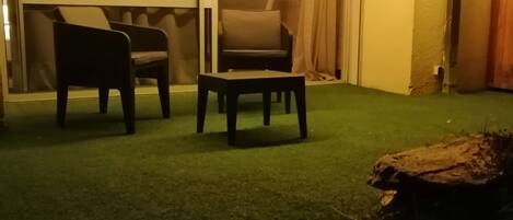 Un espacio interior con alfombra verde, dos sillas, una mesita y un banco de madera.