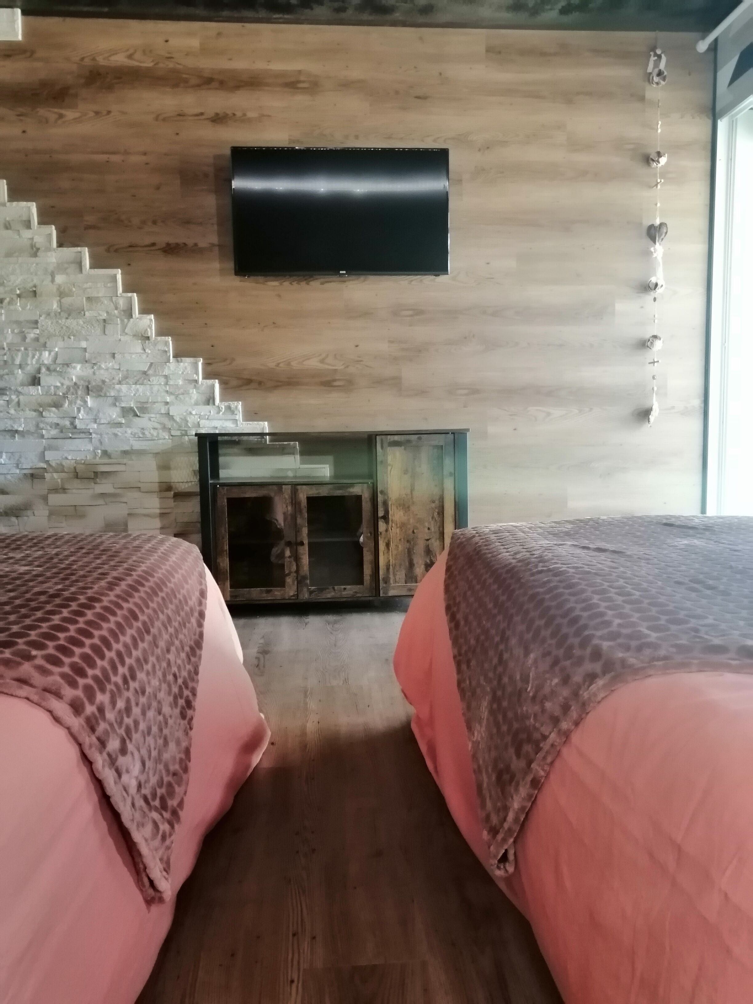 Ein Zimmer mit zwei Betten, einer Holzwand, einem Kamin und einem an der Wand befestigten Fernseher.