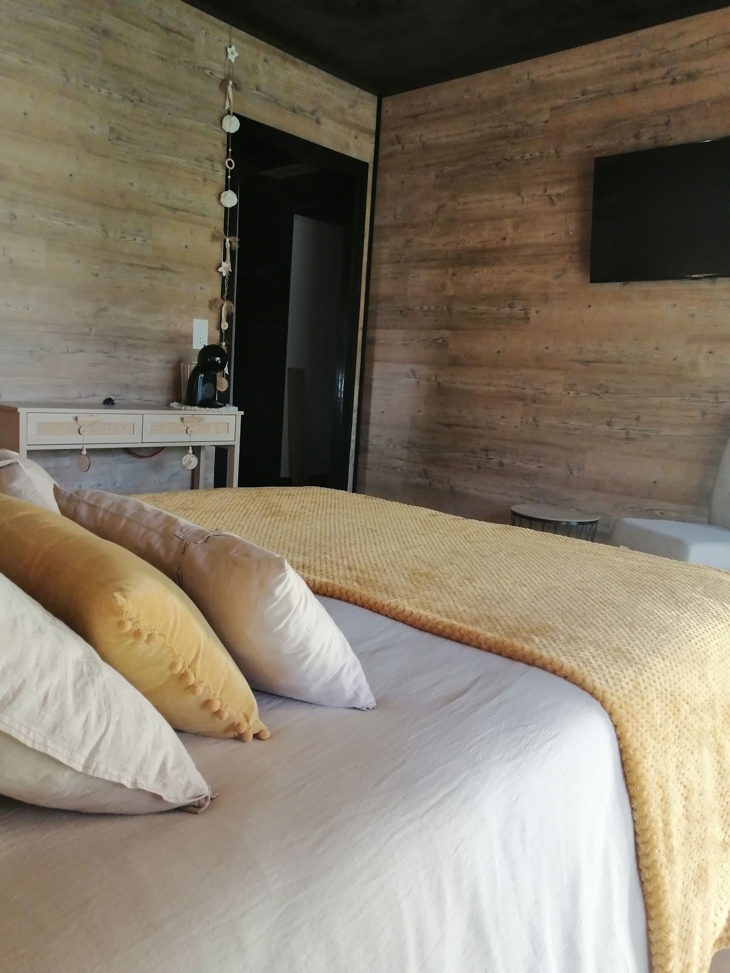Ein ordentlich bezogenes Bett mit weißer und beiger Decke, einem Holzkopfstück und einem Nachttisch mit Wasserkocher.