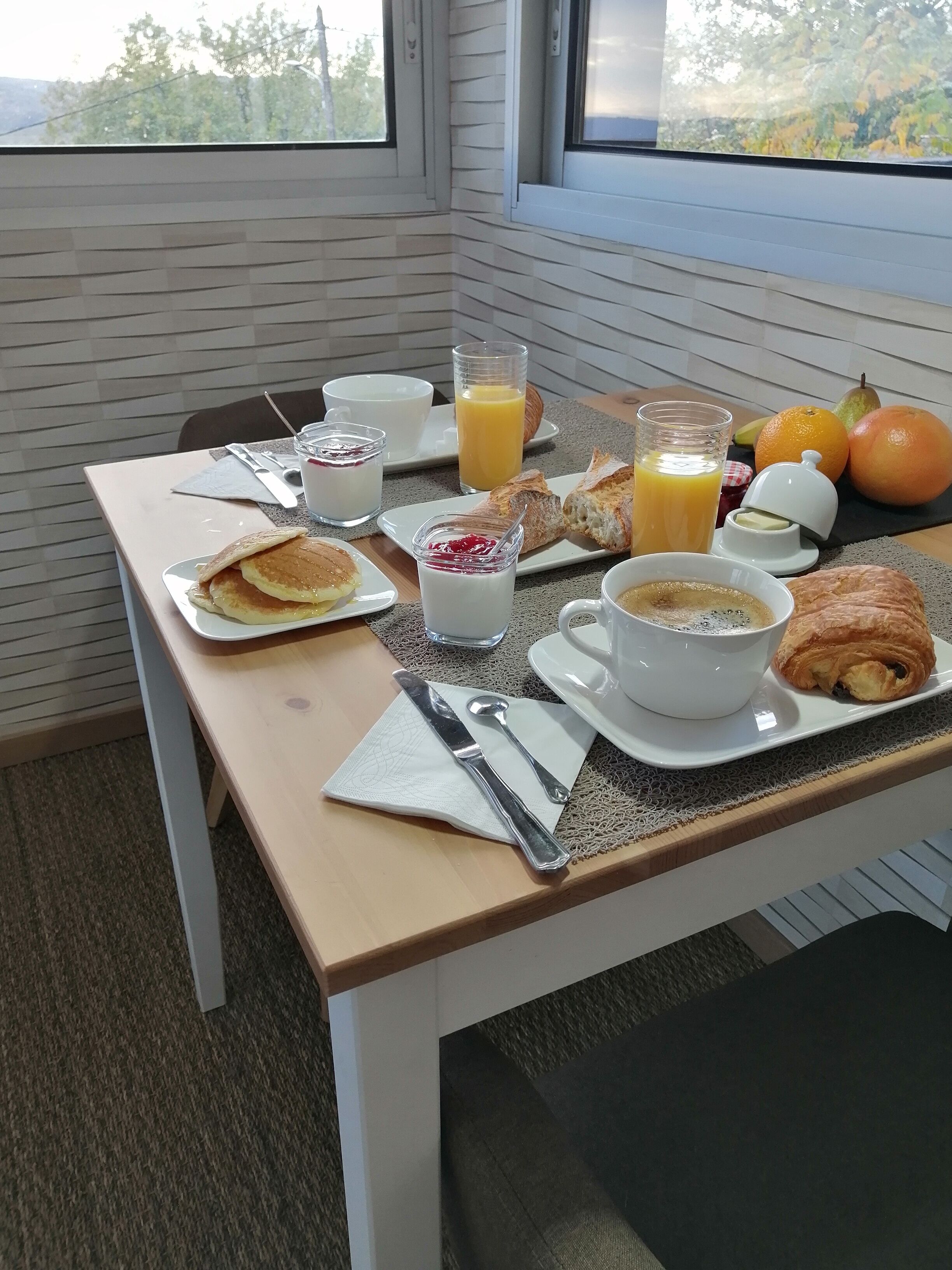 A breakfast table set with plates of pancakes, croissants, and pastries, accompanied by glasses of orange juice and coffee.