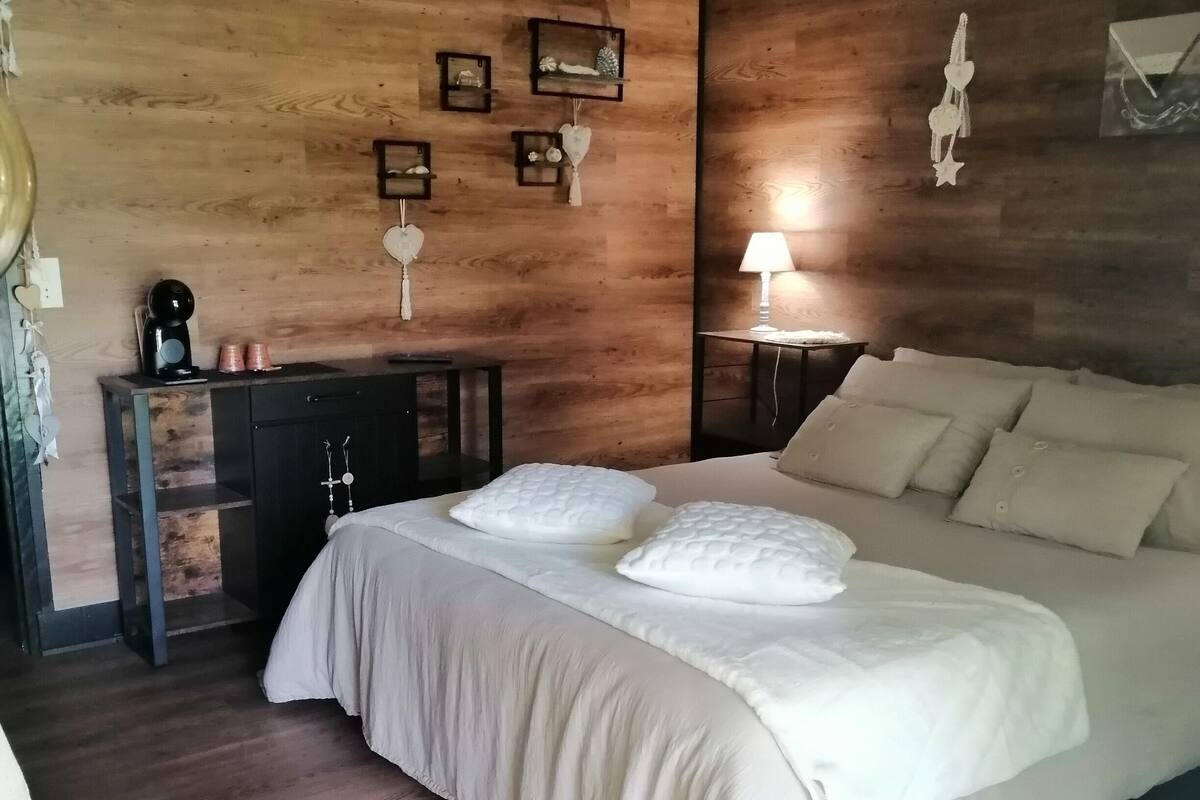 Une chambre avec un grand lit, des murs en bois, une petite table avec une lampe et une chaise.