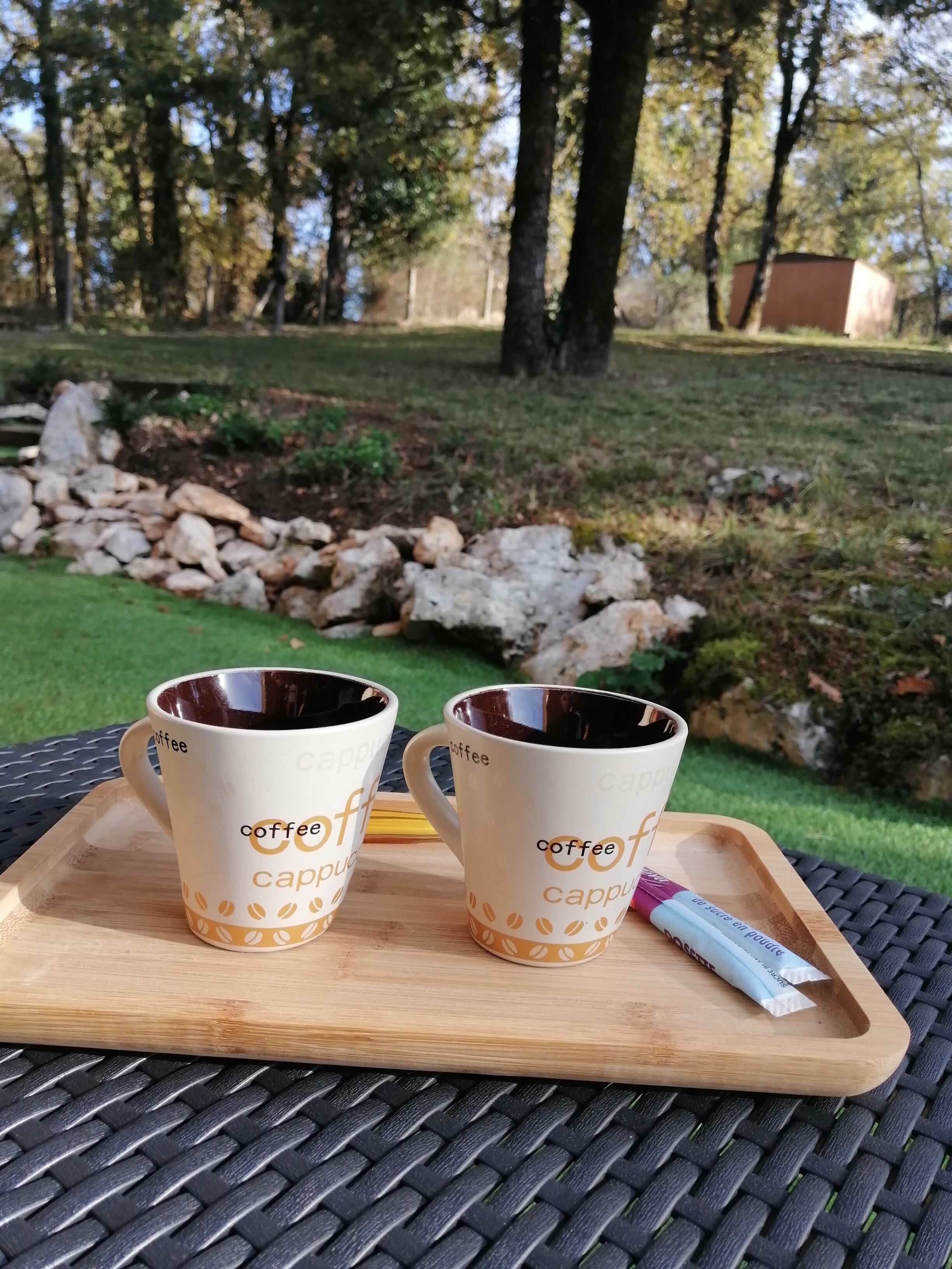 Two coffee cups on a wooden tray with a packet of coffee creamer.