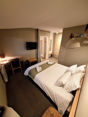 Ein Hotelzimmer mit Bett, Schreibtisch, Stuhl, Fernseher und Lampe.