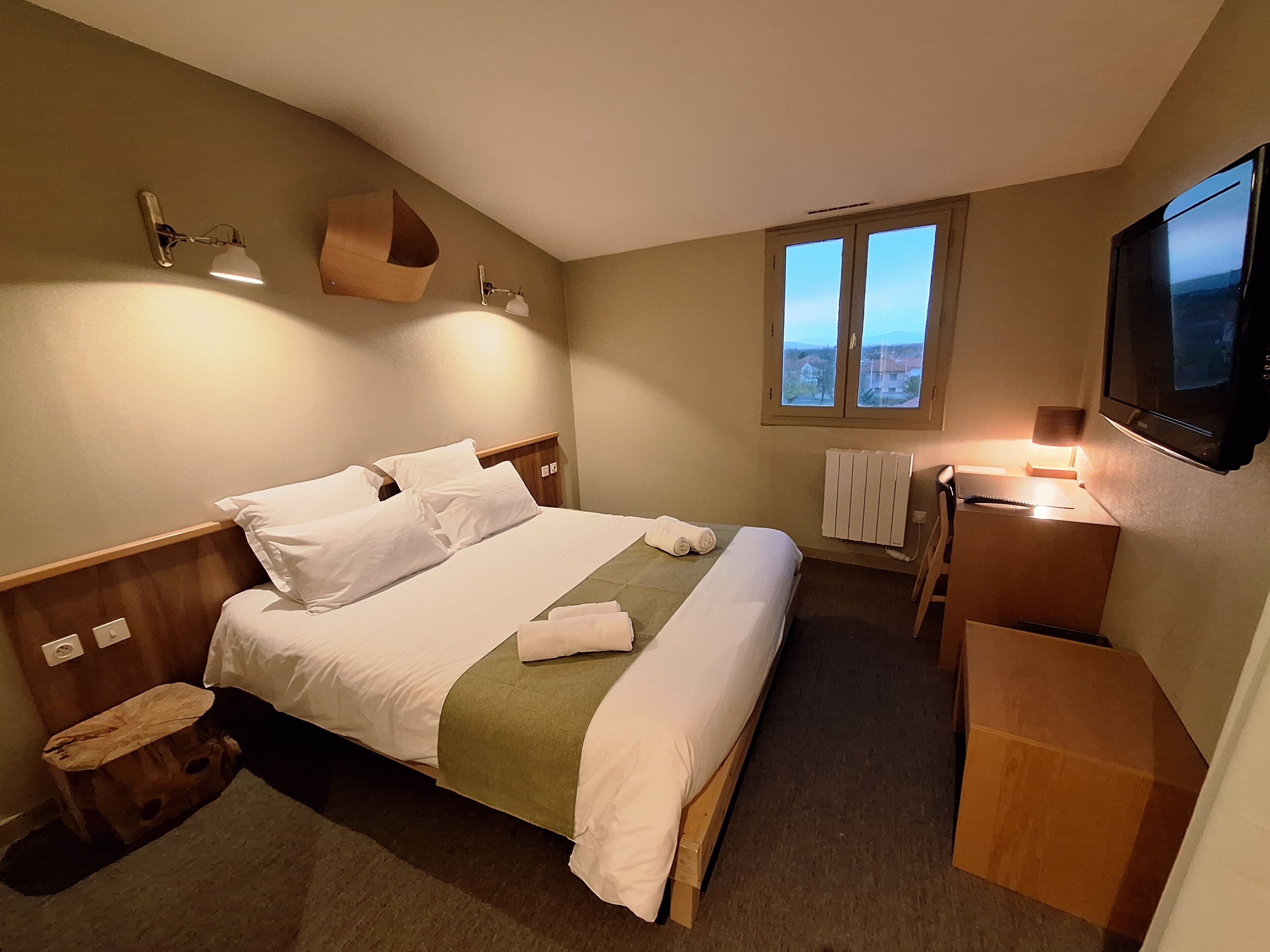 Une chambre d’hôtel équipée d’un lit, d’une table de chevet, d’une lampe et d’un téléviseur fixé au mur.