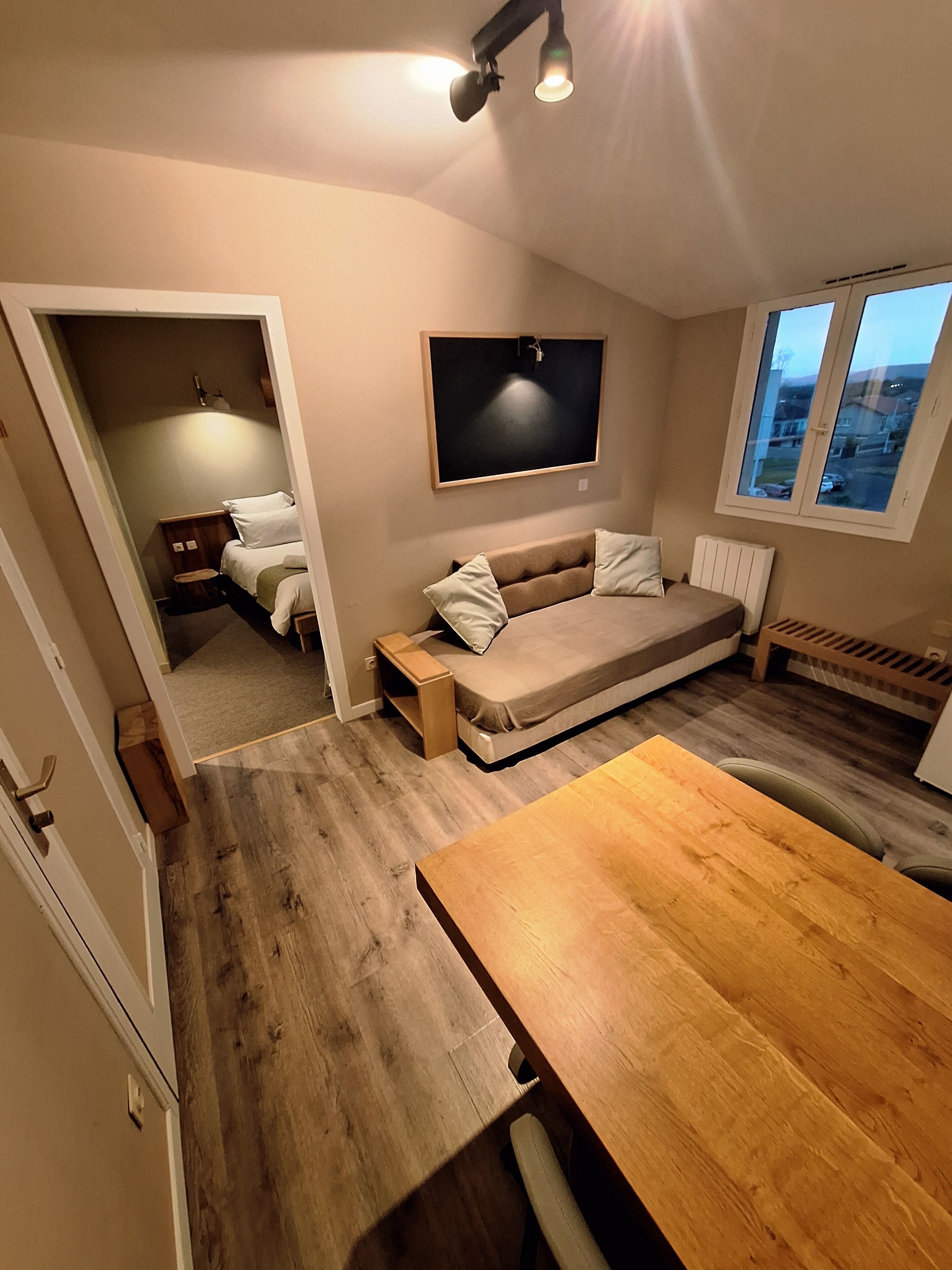 A compact room with a bed, a sofa bed, a dining table, and a TV mounted on the wall.