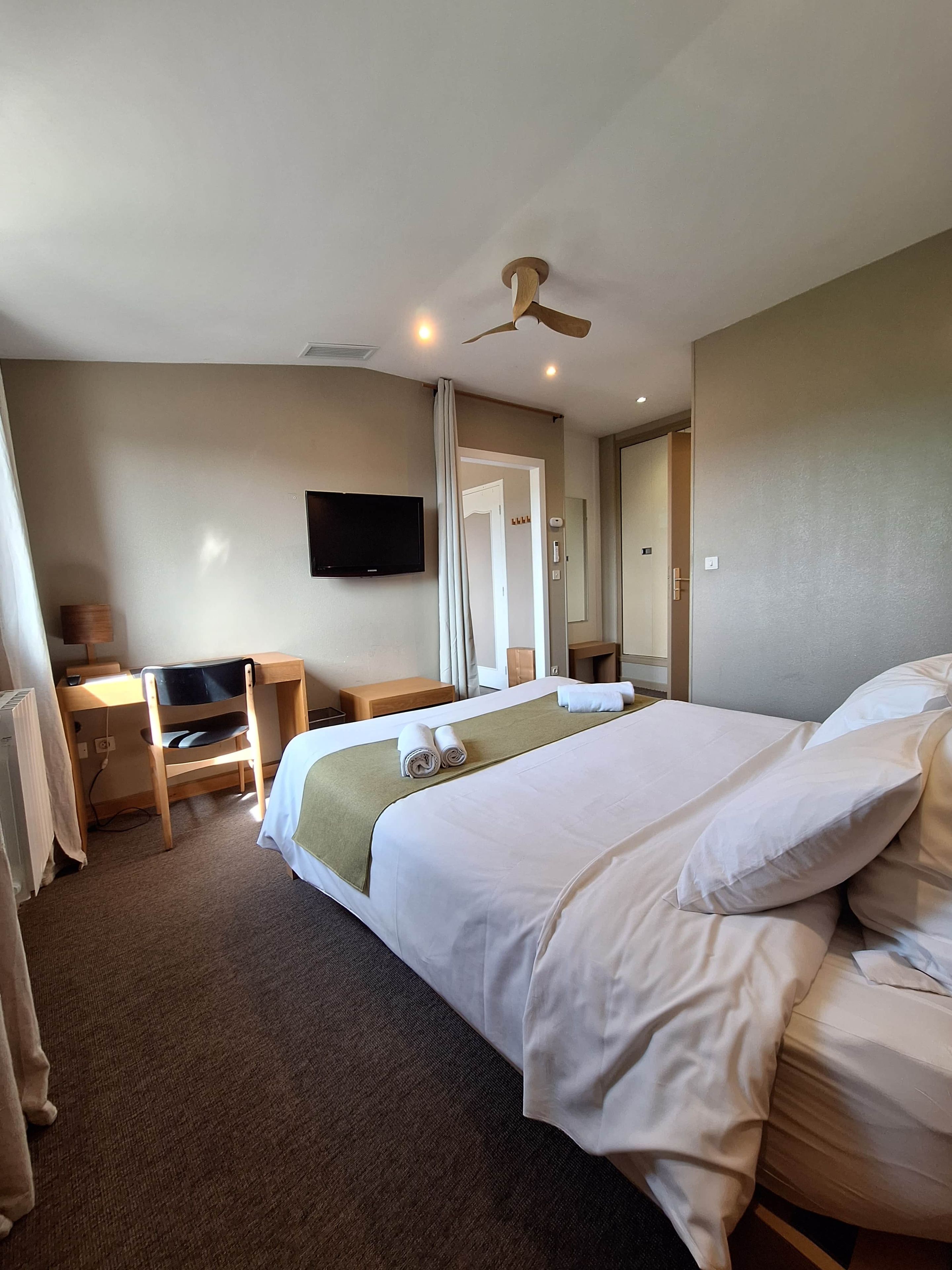 A hotel room with a bed, desk, chair, television, and a ceiling fan.