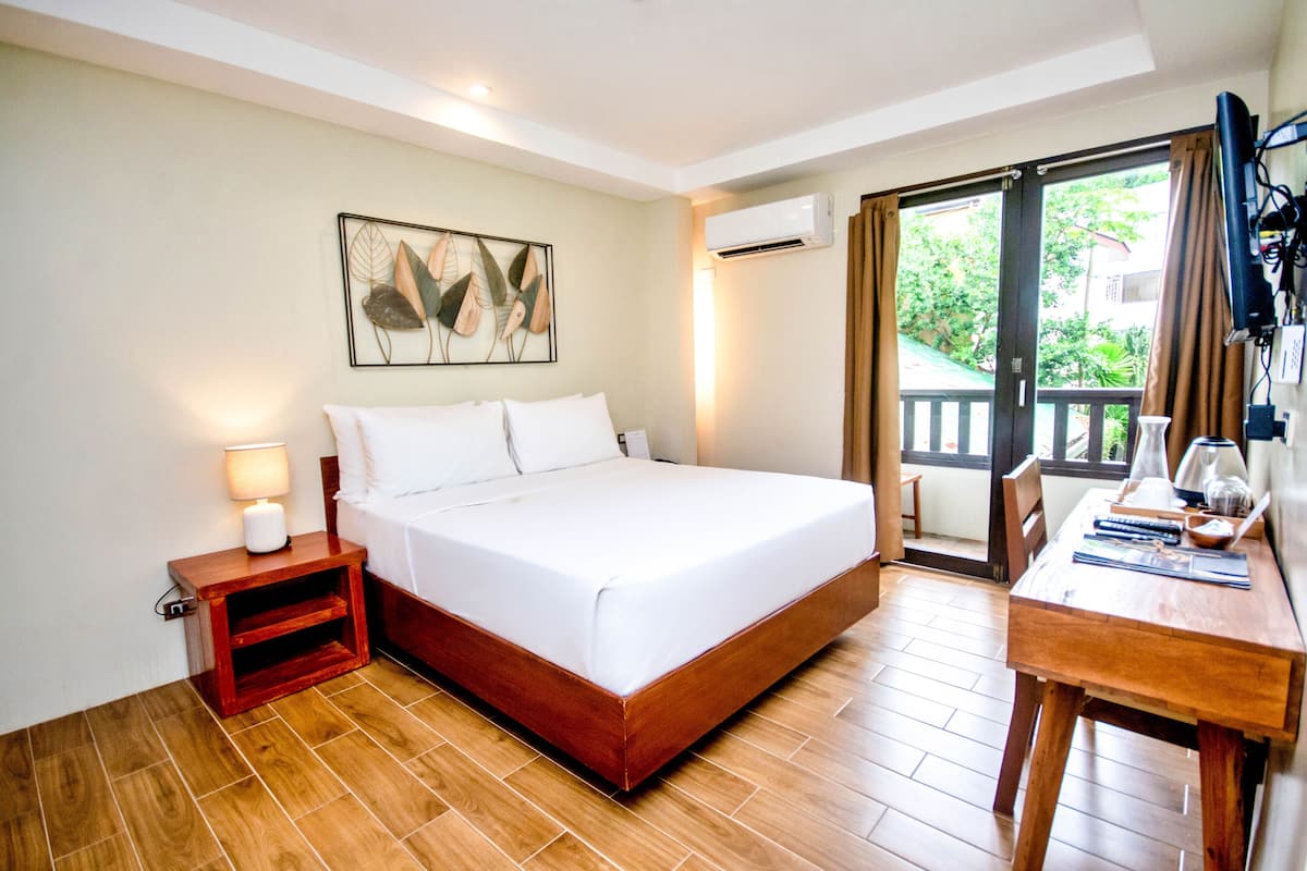 A hotel room with a bed, bedside table, lamp, and a desk with a chair.