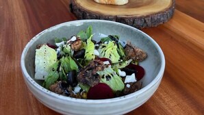 Una mesa de madera con un tazón de ensalada y dos fuentes de madera con alimentos.