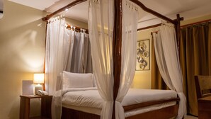 Una cama con dosel con sábanas blancas, una mesita de noche con lámpara y una silla de madera.