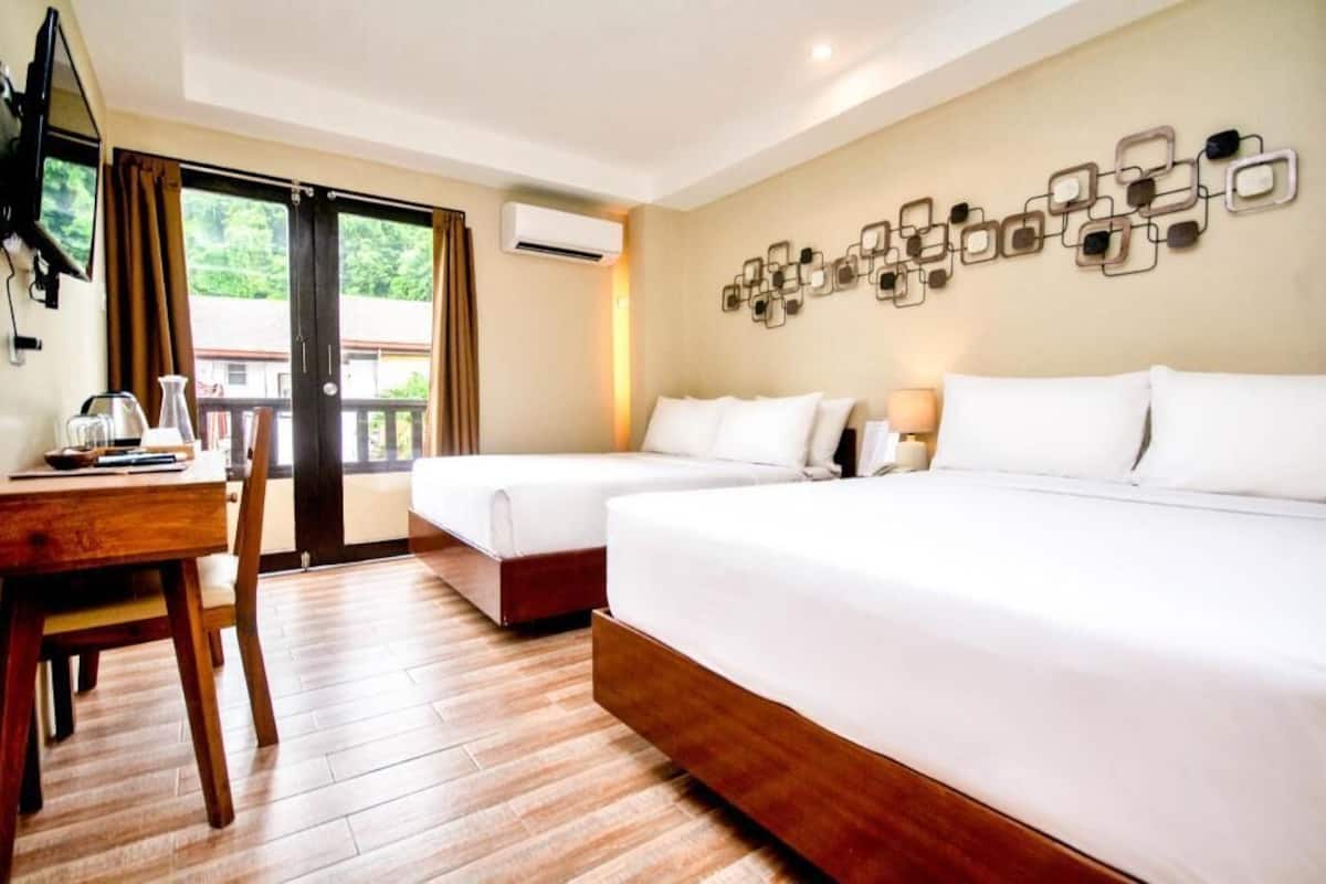 A hotel room with two beds, a desk, a chair, and a balcony with curtains.