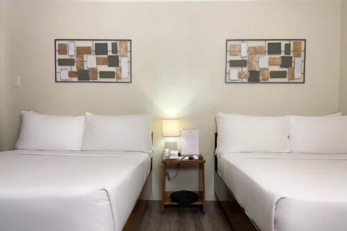 A hotel room with two single beds, a nightstand with a lamp, and two wall art pieces.
