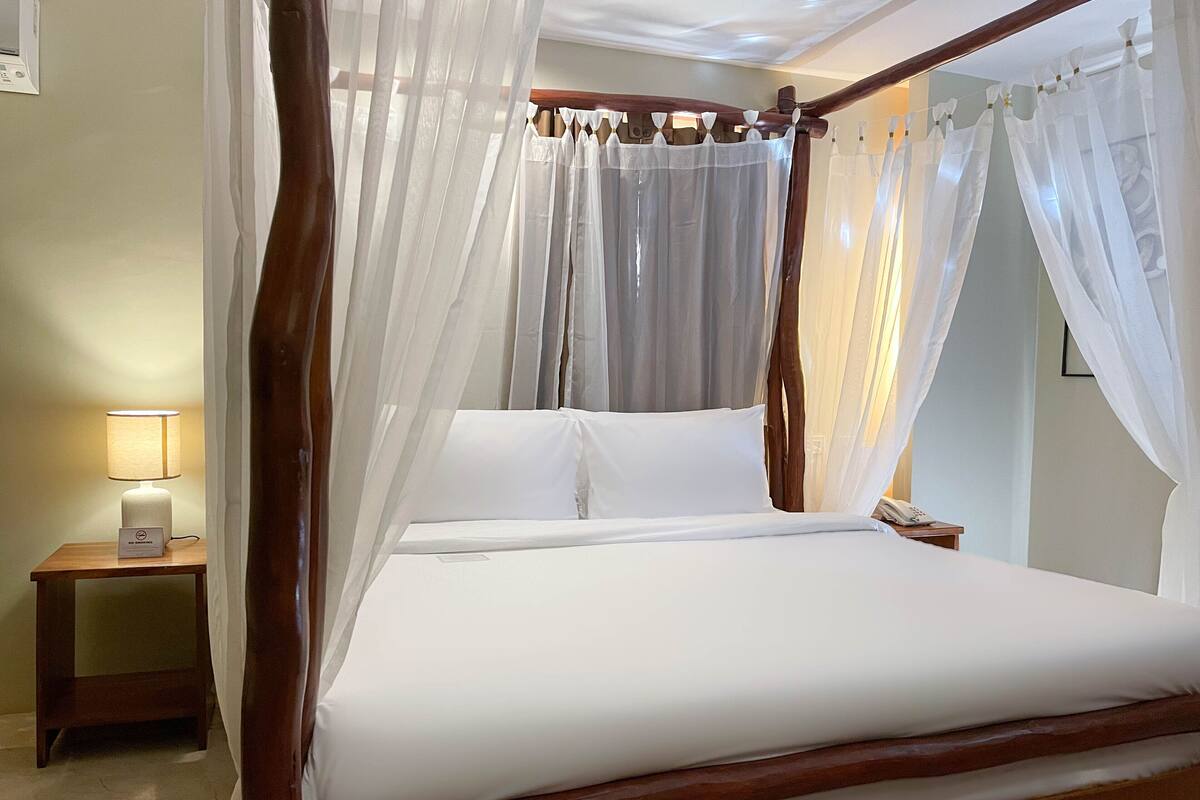 A four-poster canopy bed with white linens, a bedside table with a lamp, and a telephone.