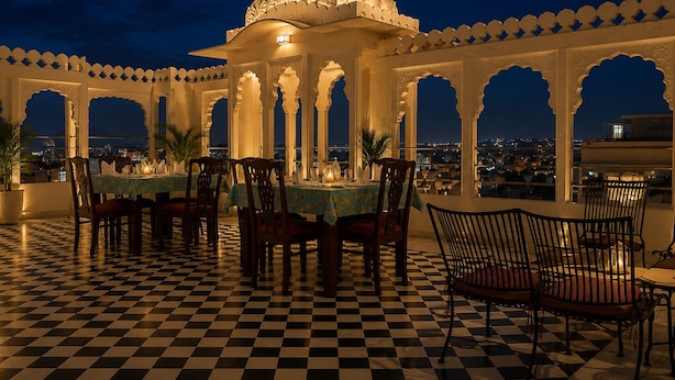 A checkered floor, a dining area with tables and chairs, and a view of the city at night. - Hotel Amar Kothi (Udaipur)
