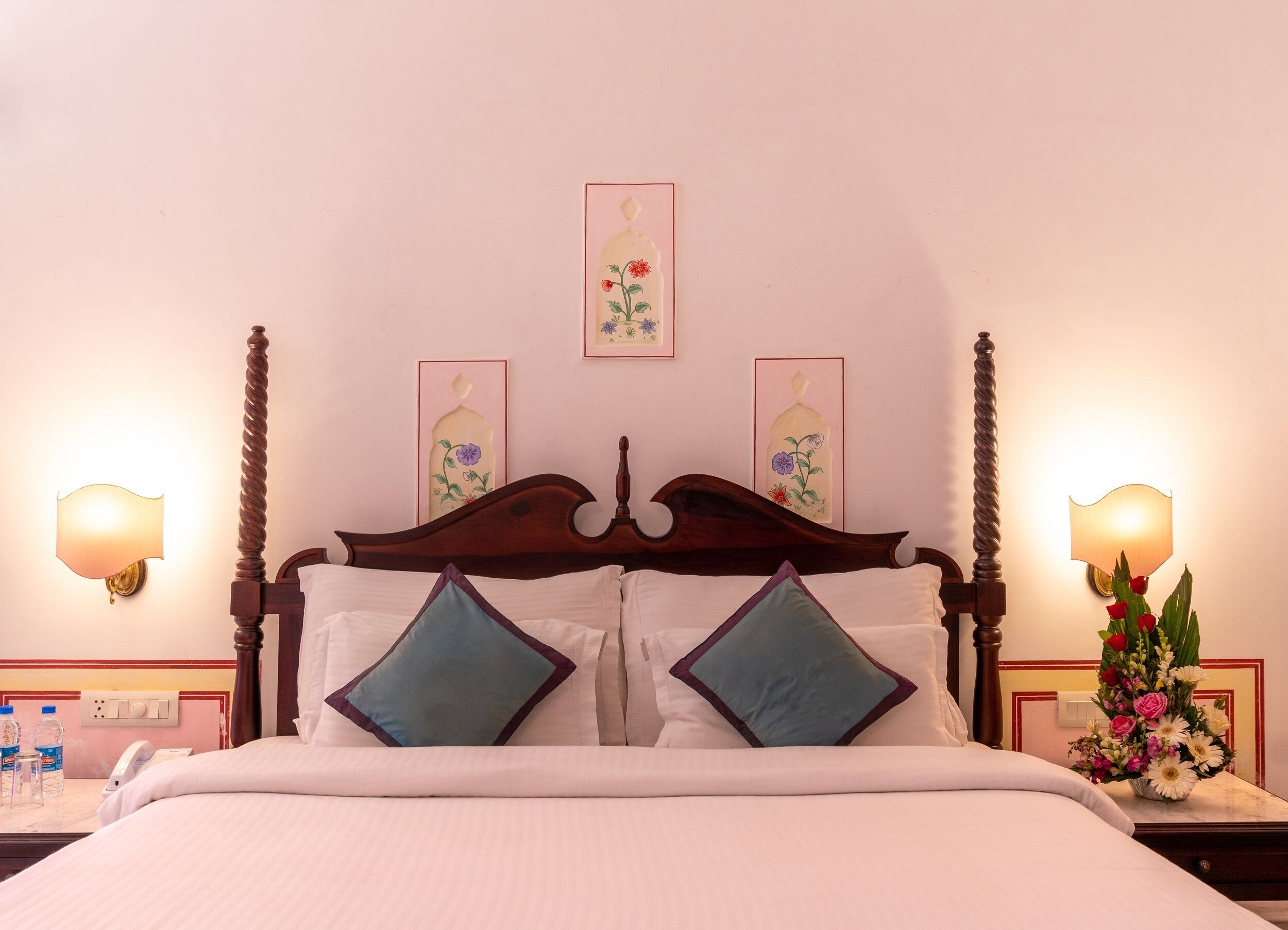 A neatly made bed with a wooden headboard, two pillows, and a vase of flowers on the nightstand.