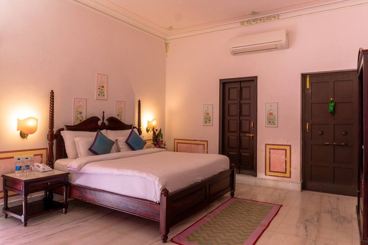 A hotel room with a large bed, bedside tables, a nightstand, a wall-mounted telephone, and a door with a handle.