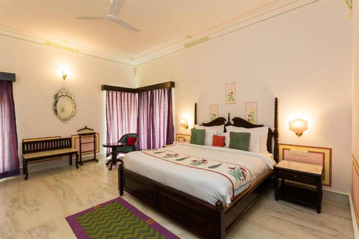 A bedroom with a large bed, a bench, a chair, and a bedside table.