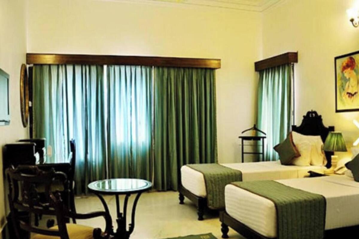 A hotel room with two beds, a small table, a chair, a lamp, and a painting on the wall.