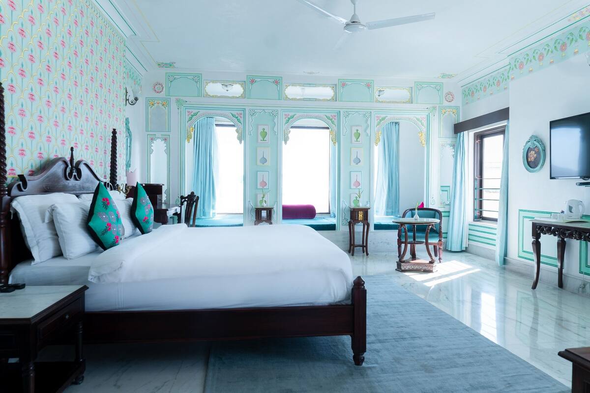 A spacious bedroom with a large bed, a ceiling fan, and a television on the wall.