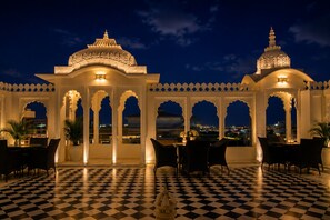 A courtyard with a checkered floor, white arches, and a view of the city at night. - Hotel Amar Kothi (Udaipur)
