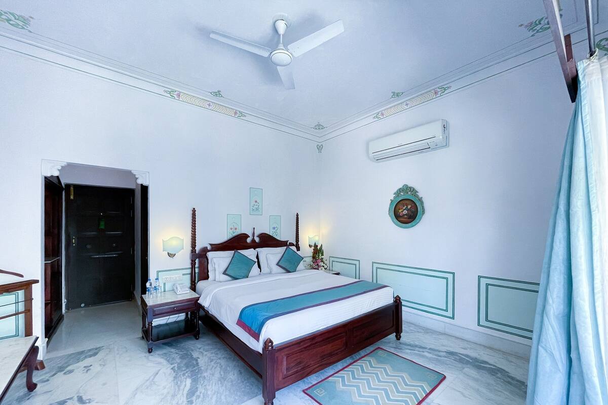 A bedroom with a bed, bedside tables, an air conditioner, a ceiling fan, and a door.