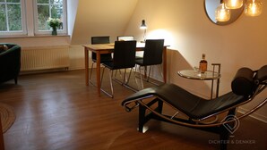 A modern loft bedroom with a sloped ceiling, a dining area with a table and chairs, a large mirror, and a lounge chair. - Vacation apartment Dichter & Denker (Weimar)