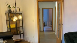 A modern living room with a sofa, a glass table, and a decorative shelf with hanging lights. - Vacation apartment Dichter & Denker (Weimar)