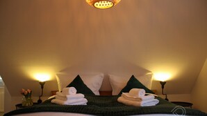 A neatly made bed with white linens and green pillows, two bedside lamps, and a vase with flowers on the nightstand. - Vacation apartment Dichter & Denker (Weimar)