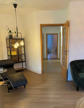 A modern living room with a sofa, a glass table, and a decorative shelf with hanging lights.