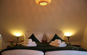 A neatly made bed with white linens and green pillows, two bedside lamps, and a vase with flowers on the nightstand.