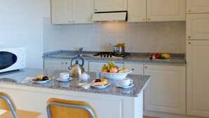 Une cuisine avec des meubles blancs, un plan de travail en granit, une bouilloire, une cuisinière et un saladier rempli de fruits.