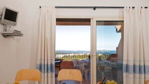 Un coin repas avec une table dressée pour deux personnes, un panier de fruits et une vue sur la mer.