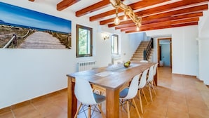 A dining area with a wooden table, chairs, and a view of a coastal landscape through a window. - Country House Finca Kiana with Pool, Garden & Wi-Fi (Sencelles)