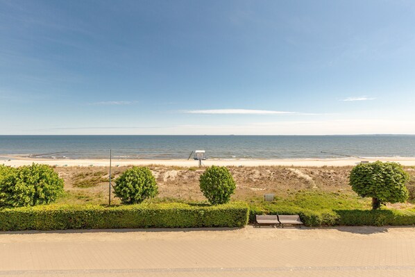 Blick auf einen Strand mit befestigtem Gehweg, einer Bank und einem Rettungsturm.