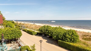 A coastal view with a beach, a pier, and a road leading to a building with outdoor seating. - Dünenresidenz, App. A14 (Heringsdorf)