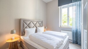 A modern bedroom with a large bed, two bedside tables, and a window with curtains. - Villa Goodewind, App. 1.1 (Heringsdorf)