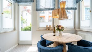 A room with a round wooden table, two blue chairs, a vase with flowers, and a bottle of wine. - Villa Goodewind, App. 1.1 (Heringsdorf)