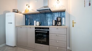 A compact kitchen with a refrigerator, oven, and coffee maker. - Villa Goodewind, App. 1.1 (Heringsdorf)