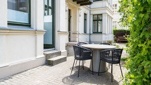 A patio with a round table and chairs, a wooden bench, and a small garden area. - Villa Goodewind, App. 1.1 (Heringsdorf)