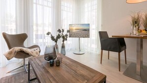 Un soggiorno moderno con un tavolino in legno, due poltrone, una TV su un mobile basso e un'ampia finestra con tende leggere.