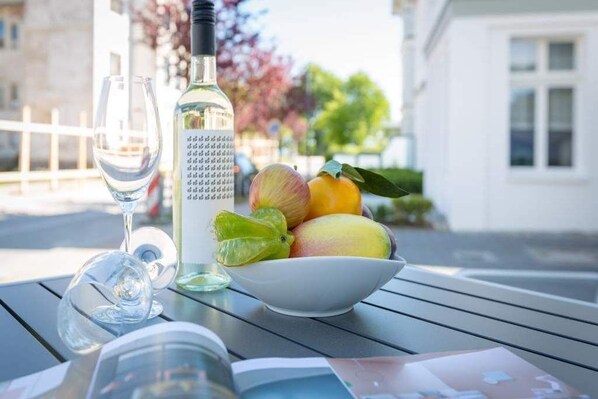 A table with a bottle of white wine, a glass, and a bowl of fruit.