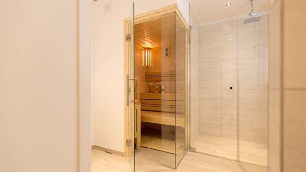 Un bagno moderno con sauna in vetro, zona doccia e una panca in legno.