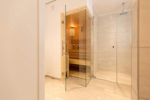 A modern bathroom with a glass-enclosed sauna, a shower area, and a wooden bench.