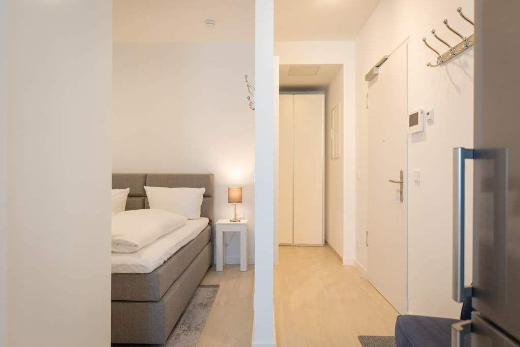 Une chambre à coucher avec un lit, une table de chevet et une lampe. Un couloir mène à une porte.