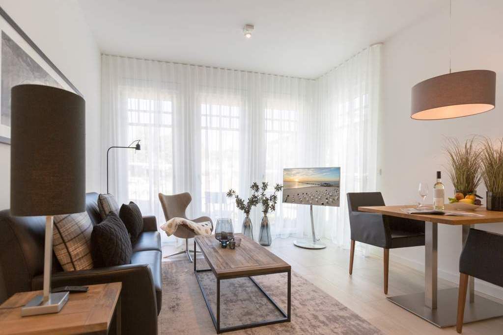 Ein modernes Wohnzimmer mit Sofa, Couchtisch und Essbereich. An der Wand hängt ein Gemälde, auf dem Tisch steht eine Lampe und eine Pflanze.