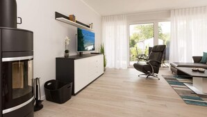A modern living room with a flat-screen TV, a black sofa, a black chair, and a wooden floor. - Villa Strandgrün, App. 04 (Heringsdorf)