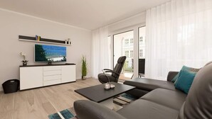 A modern living room with a flat-screen TV, a sofa, a coffee table, and a view of the outside. - Villa Strandgrün, App. 04 (Heringsdorf)
