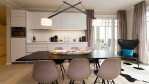Une cuisine moderne avec des meubles blancs, une table à manger avec des chaises et un canapé noir agrémenté d’un coussin bleu.