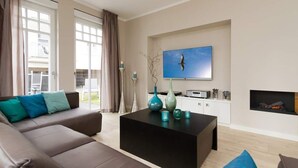 Un salon moderne avec un canapé, une table basse, un téléviseur, une cheminée et de grandes fenêtres.