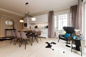 Ein modernes Wohnzimmer mit Essbereich, einem schwarzen Ledersessel, einem Glastisch und einem Kuhfellteppich.